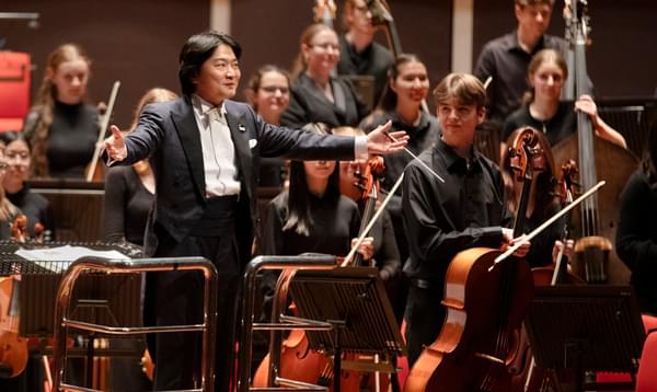 Conductor with wide open arms standing in front of an orchestra