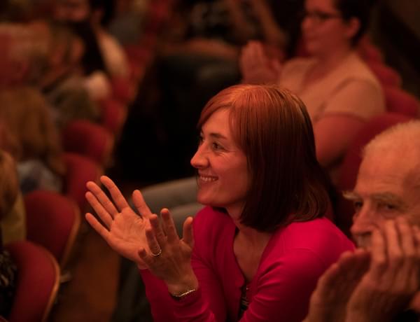 Photograph of a woman smiling and clapping in Symphony Hall