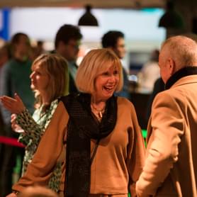 Photograph of a woman smiling and talking to a friend in the Symphony Hall foyer