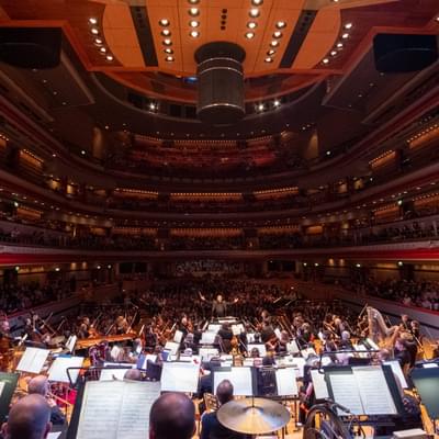 Photograph of the full orchestra on-stage at Symphony Hall, with a packed auditorium visible behind them