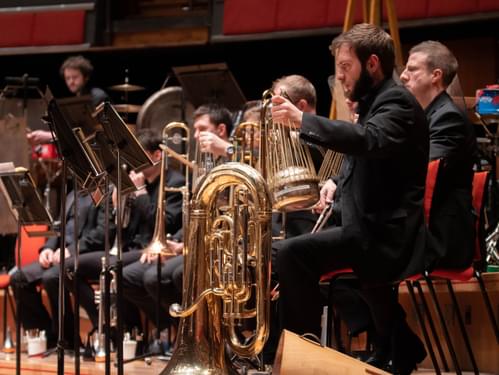 Photograph of a tuba player using his mute as a percussion instrument.