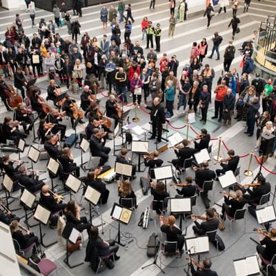 Photograph of the full orchestra from above performing at New Street station