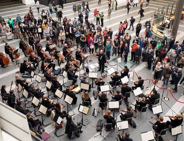 Photograph of the full orchestra from above performing at New Street station