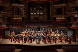 Photograph of the full orchestra standing on-stage at Symphony Hall and smiling
