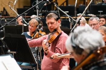 Photograph of viola player Adam Romer and other string players recording whilst wearing headphones