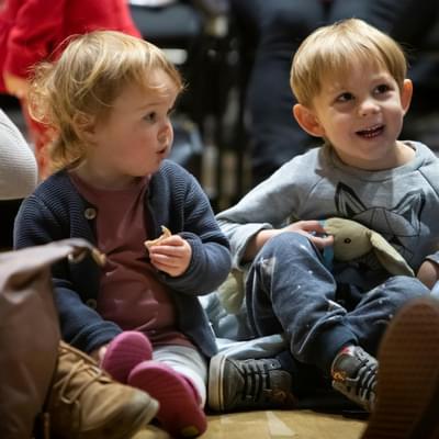 Two young children are smiling and sitting on the floor
