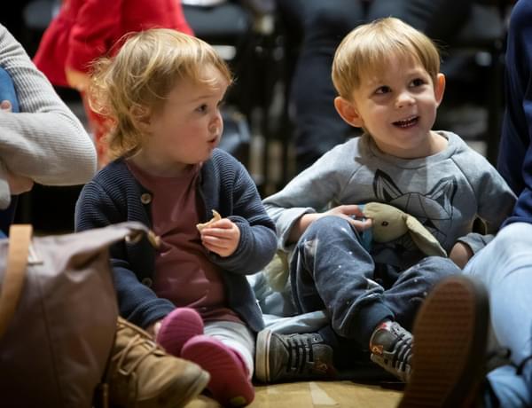 Two young children are smiling and sitting on the floor