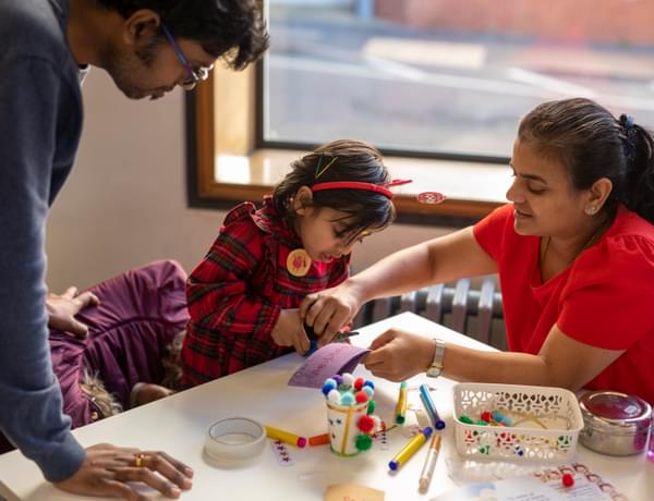 Photograph of a young girl being helped with craft by her mother and father