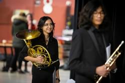 Photograph of a teenage girl holding a French Horn waiting to go on-stage at Symphony Hall for a Project Remix performance