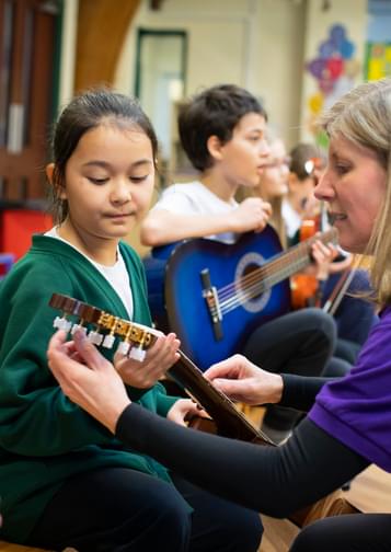 Photograph of Jane Wright helping a young girl in school uniform to tune a guitar.