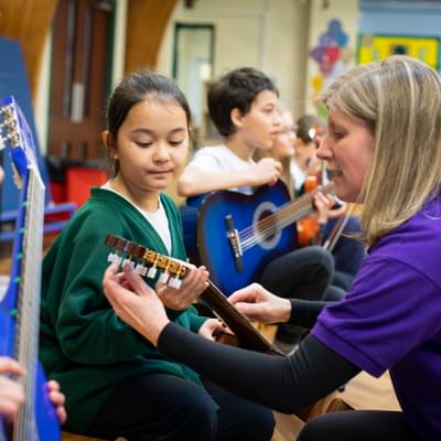 Photograph of Jane Wright helping a young girl in school uniform to tune a guitar.