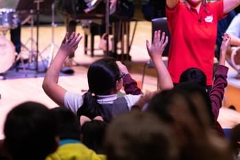 Photograph of a child holding their hands above their head as they watch a Relaxed Concert