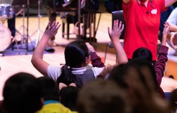 Photograph of a child holding their hands above their head as they watch a Relaxed Concert