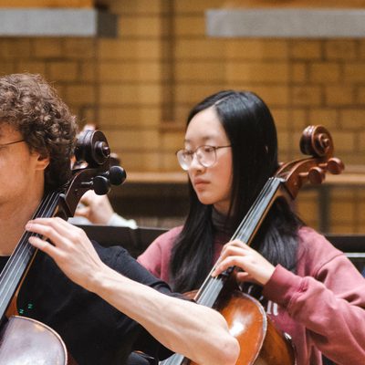 Photo of three young cellists playing in a rehearsal.