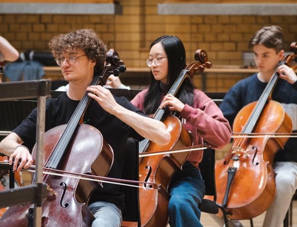 Photo of three young cellists playing in a rehearsal.