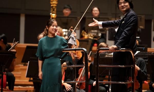 conductor pointing to a solo violinist in a green dress