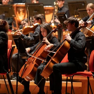 young musicians playing the cello in an orchestra on a stage