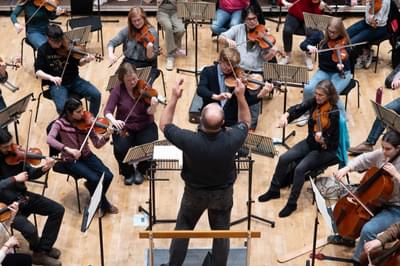 conductor leading a group of violinists at the front of an orchestra