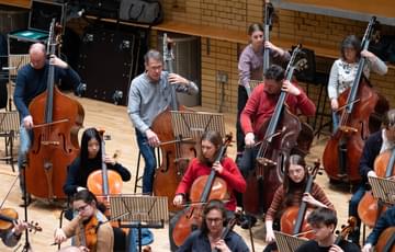 four double bass players sat with cellos in an orchestra