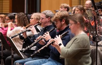 Oboes and Flutes sat next to each other playing in an orchestra
