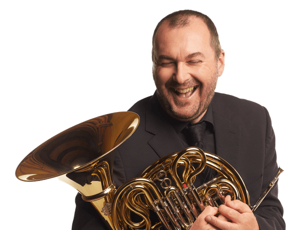 Headshot of french horn player Jeremy Bushell. Jeremy is laughing and is holding his french horn to his chest.