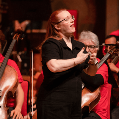 Photo of BSL Interpreter Sarah Butt on stage. Sarah is stood in front of some musicians signing.