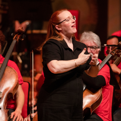 Photo of BSL Interpreter Sarah Butt on stage. Sarah is stood in front of the orchestra signing.