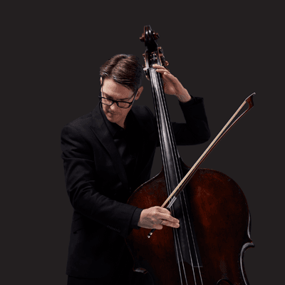 Photograph of Jeremy Watt playing the double bass on a black background.